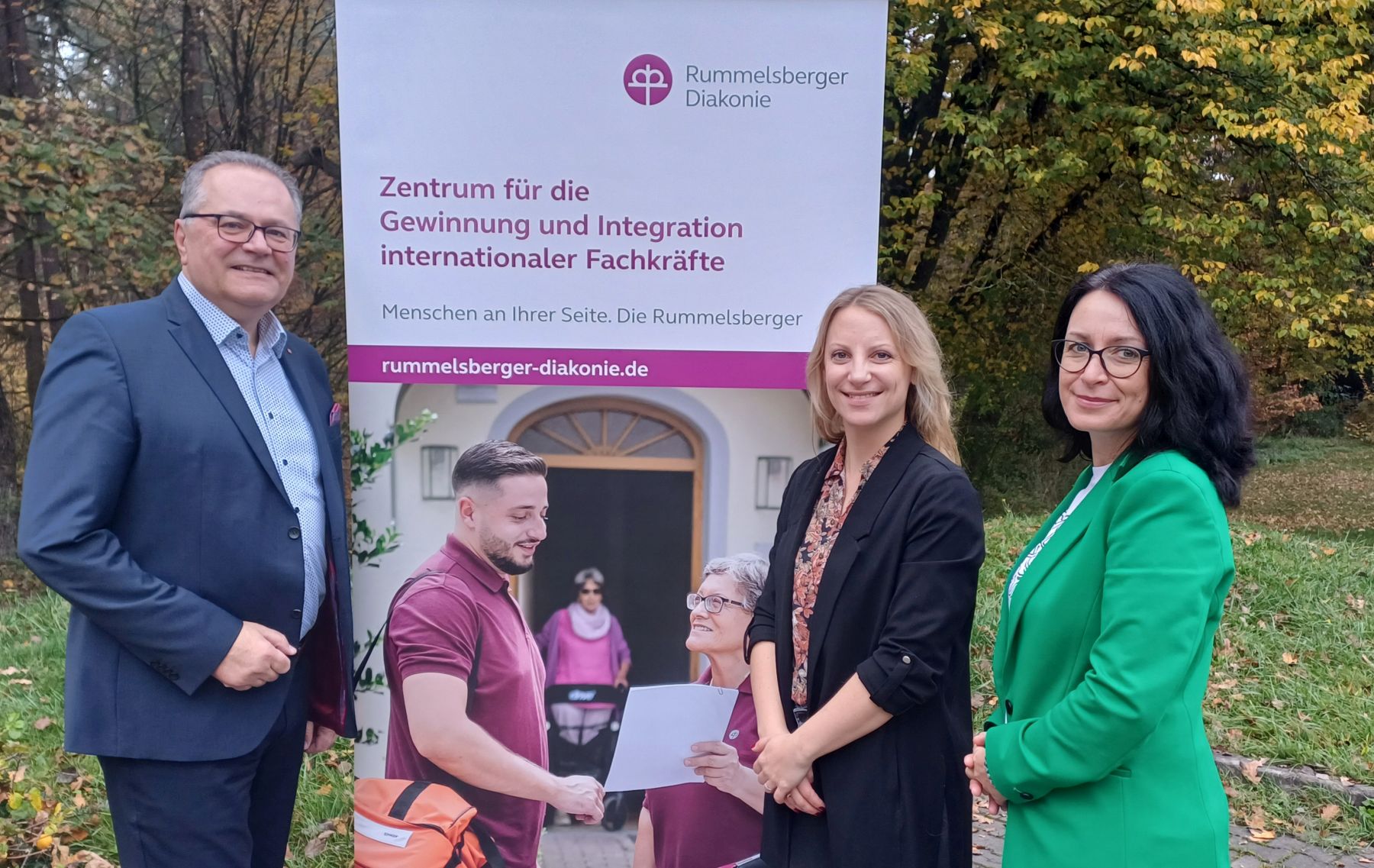 Ein Mann und zwei Frauen stehen vor einem Poster