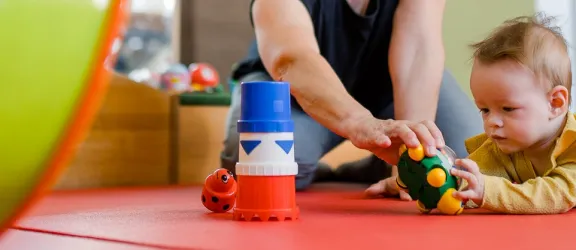 Baby bei der Frühförderung liegt auf dem Boden und greift ein Spielzeug