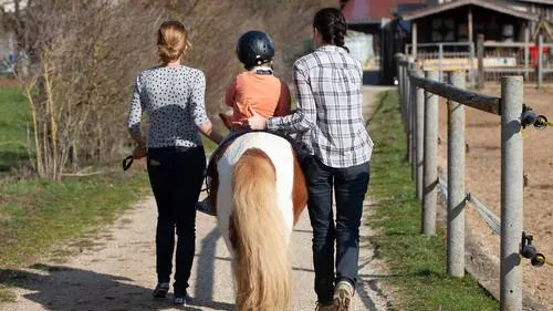 Kind reitet auf Pferd. Zwei Erwachsene begleiten