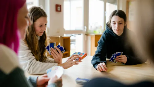 Zwei Mädchen und eine Mitarbeitende spielen Karten